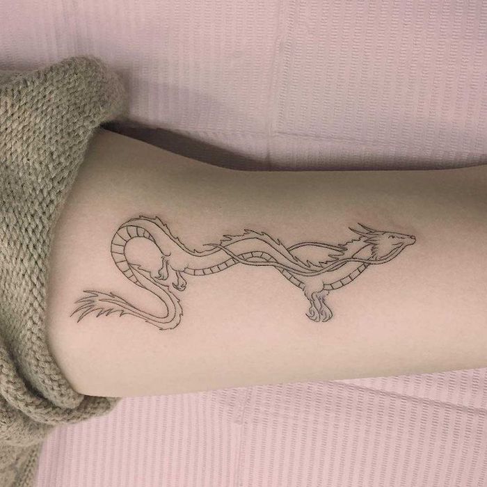 hand leaning on pink paper, woman wearing beige sweater, forearm tattoo, red dragon tattoo