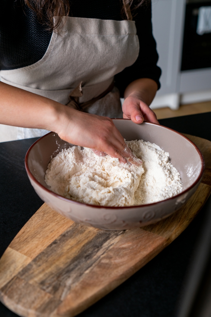 dry and wet ingredients in ceramic bowl, naan bread, mixed together to form dough, wooden cutting board