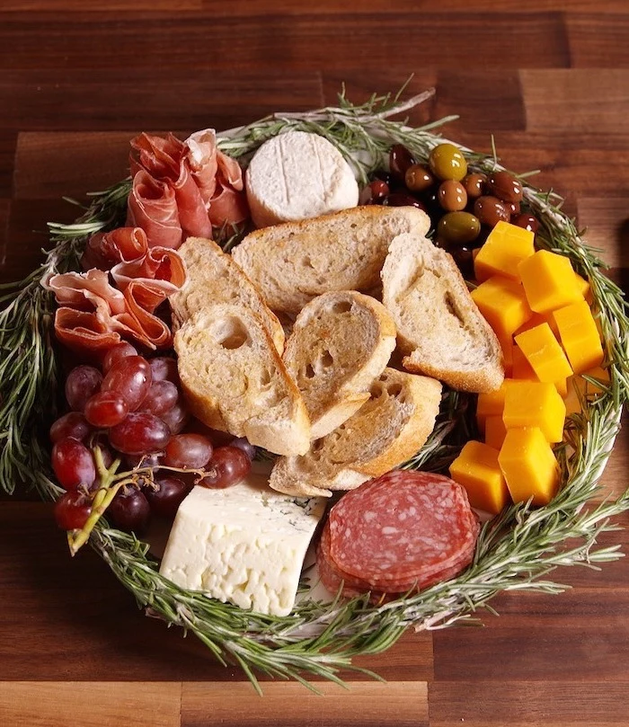 christmas appetizer recipes, wreath made of rosemary, different types of cheese and meat, olives and bread, placed on wooden surface