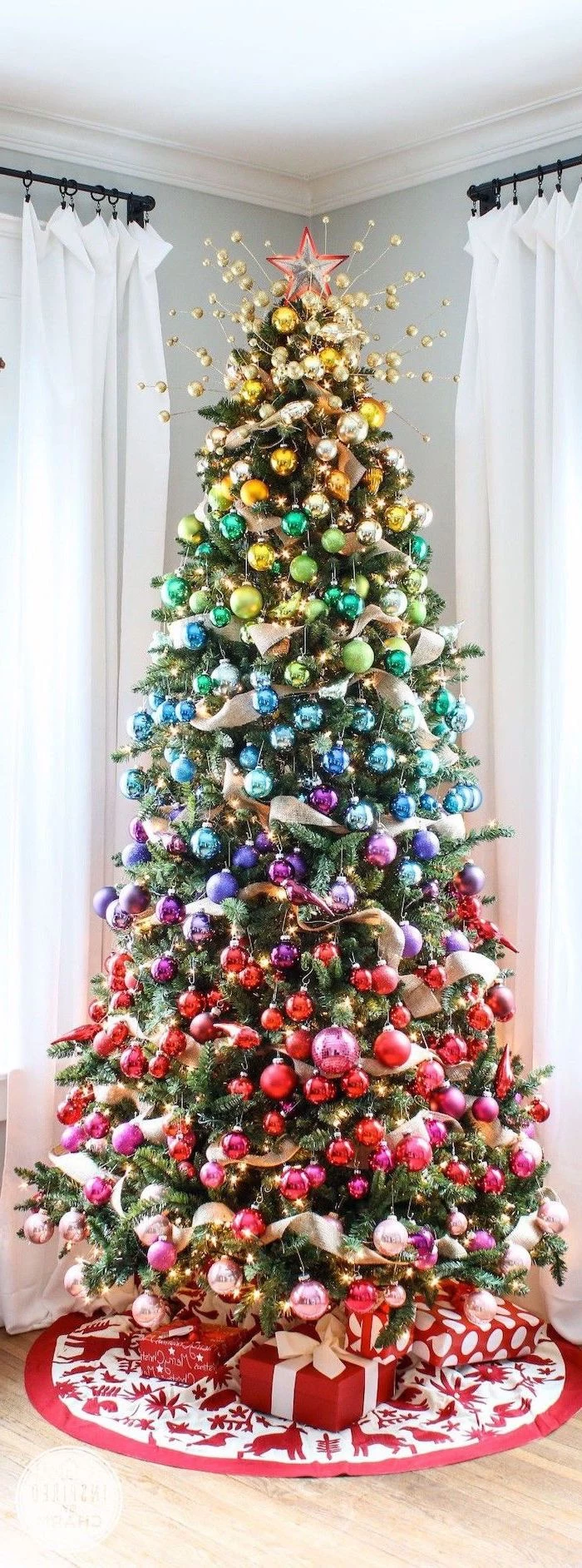 tall tree decorated in gradients colors of the rainbow, christmas tree ribbon, wrapped presents underneath