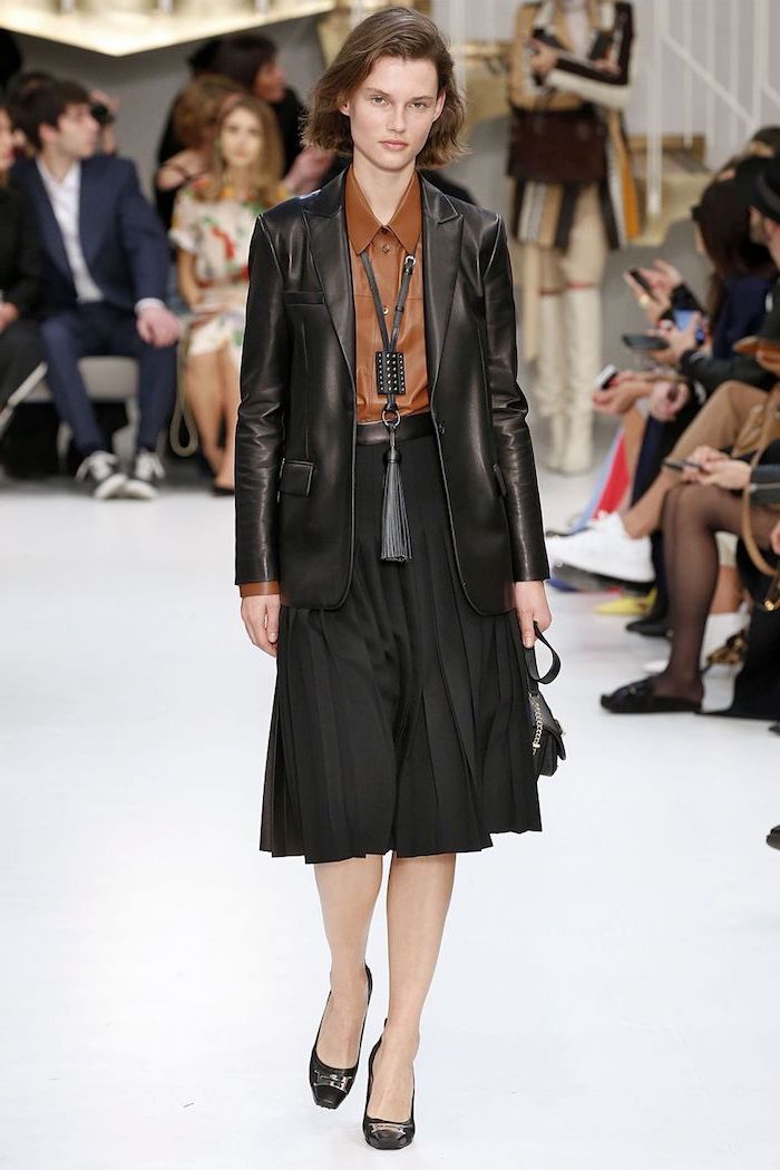 model walking down a runway, wearing black plaid skirt and blazer, new fashion trends, brown leather shirt and black heels