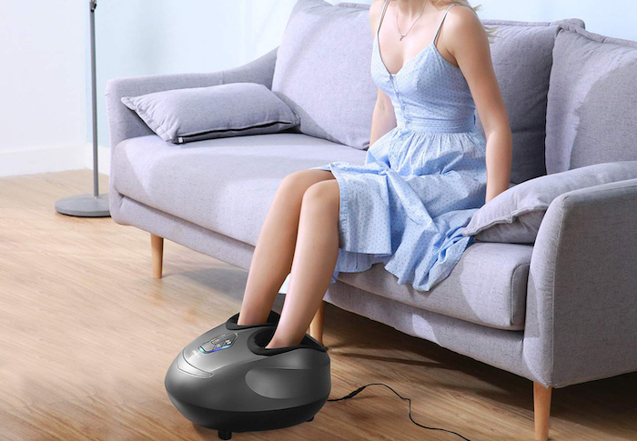 woman wearing blue dress, sitting on grey sofa, using a foot massager, what to get your mom for christmas, wooden floor