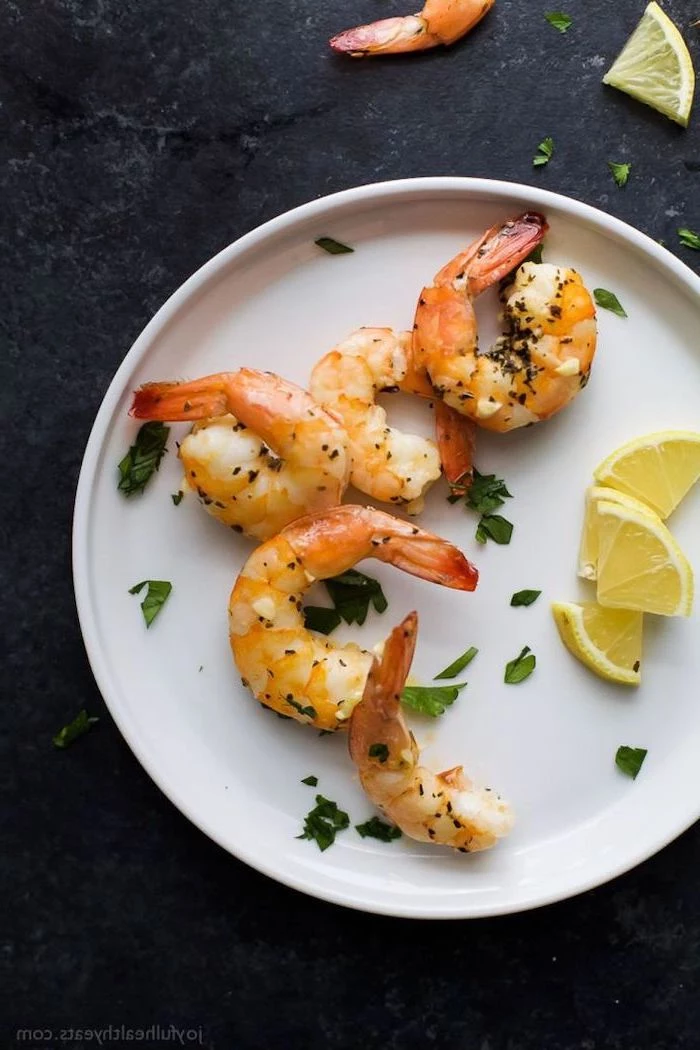 garlic and herb roasted shrimp on white plate, lemon slices on the side, christmas party finger foods, placed on black surface