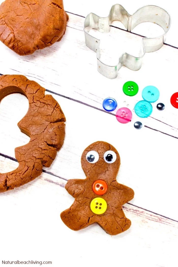 gingerbread man made out of play dough, christmas craft ideas for kids, colorful buttons placed on white wooden surface