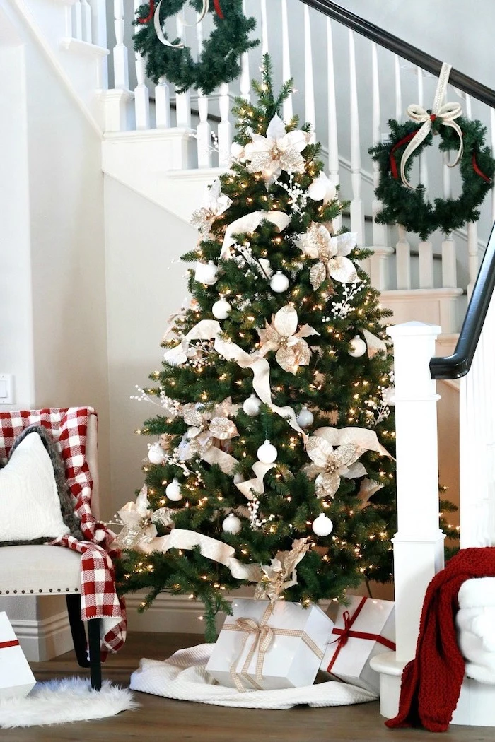 tree decorated with white flowers and ornaments, rose gold christmas tree, wrapped presents underneath, next to the staircase