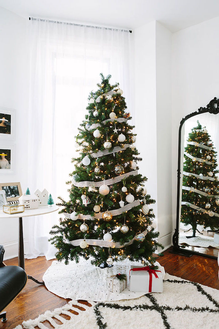 tree placed on white rug, decorated with white ribbon and ornaments, rose gold christmas tree, on wooden floor