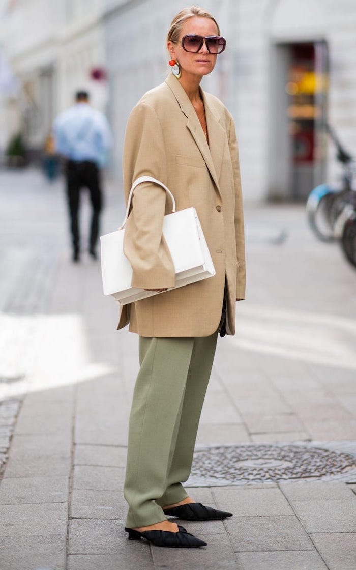 woman with sunglasses and blonde hair, wearing green pants and oversized blazer, new fashion trends, carrying white bag