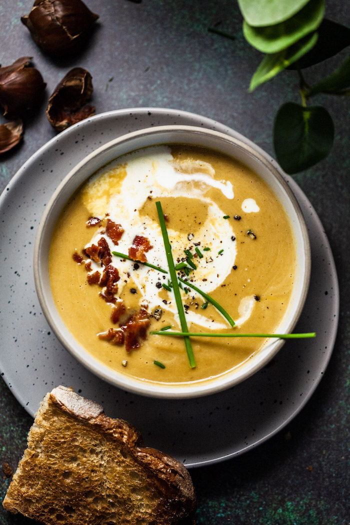 grey ceramic bowl full of soup with bacon on top, old fashioned potato soup, bread on the side on a grey countertop