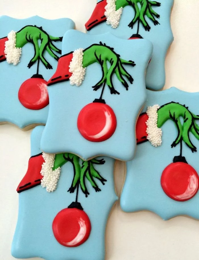 grinch cookies, decorated with blue red and green icing, the grinch's hand holding an ornament, how to make icing for cookies