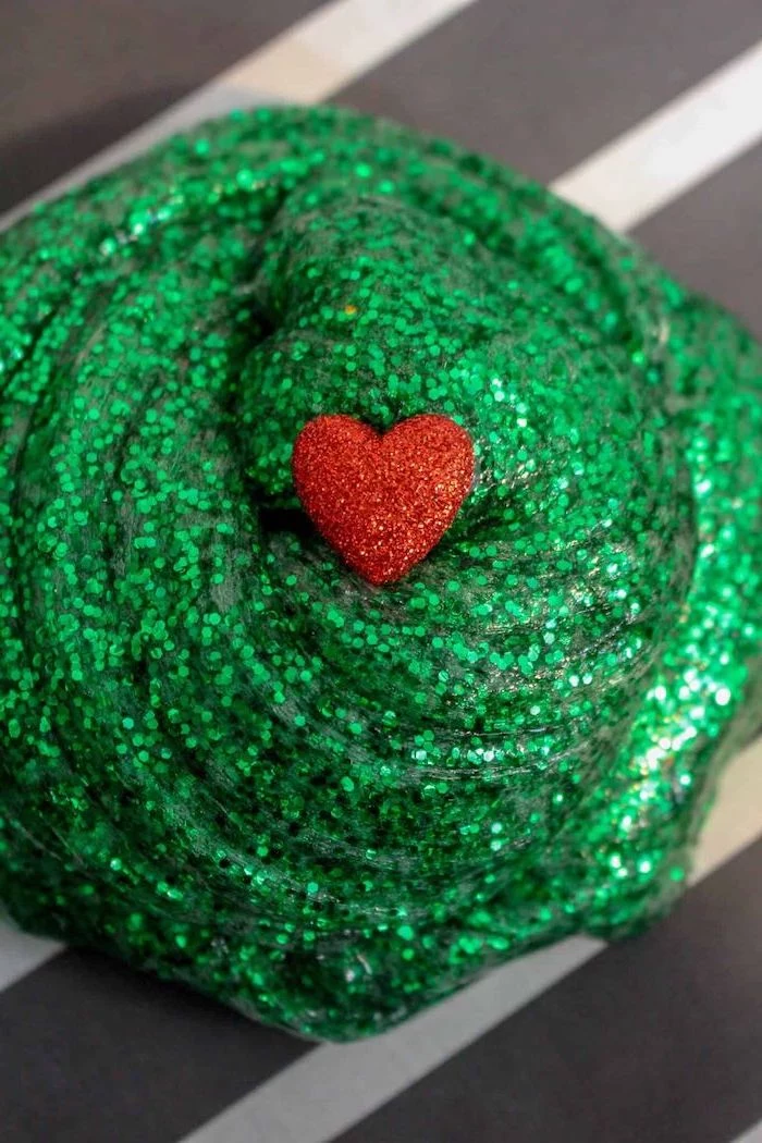 grinch slime made of green glitter, christmas craft ideas for kids, red glittery heart on top