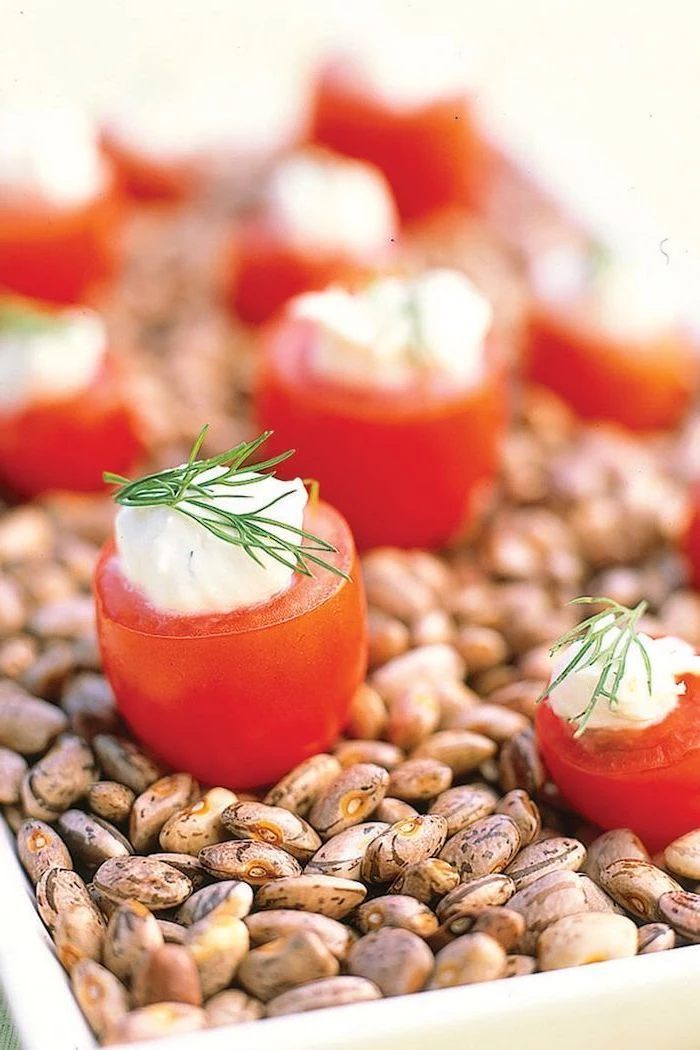 halved cherry tomatoes, sour cream inside and dill on top, christmas party finger foods, placed on bowl full of beans