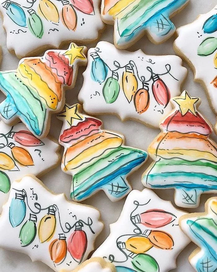 christmas tree shaped cookies, how to make icing for cookies, hand painted as trees and hanging lights, placed on white surface
