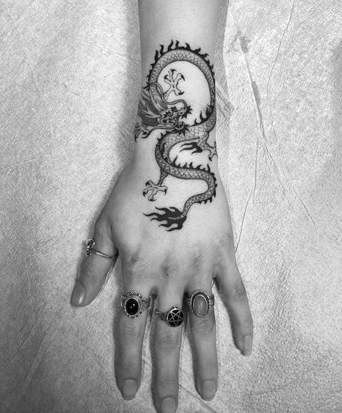 black and white photo, dragon sleeve tattoo, wrist tattoo, hand with los of rings on it, white background