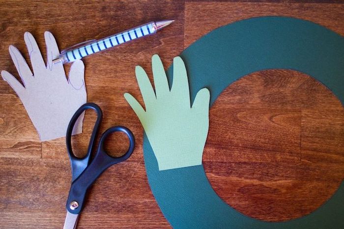 pen and scissors, handprint cut out of green paper, homemade christmas crafts, placed on wooden surface