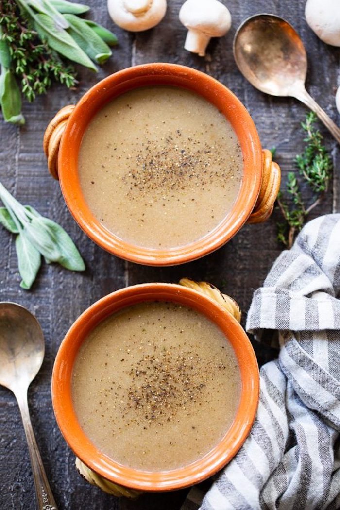 creamy tortellini soup, two orange ceramic bowls full of soup, fresh herbs around them, arranged on black wooden table