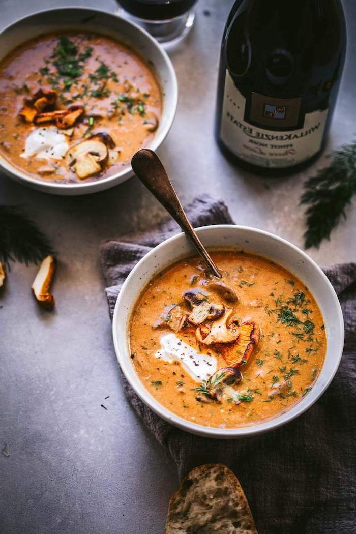 two ceramic bowls full of soup, mushrooms and fresh herbs on top, creamy tortellini soup, wine bottle on the side