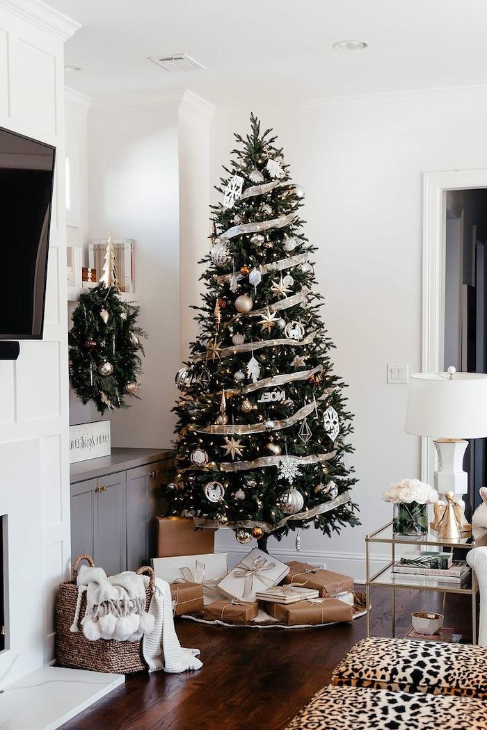 decorating christmas tree with ribbon, gold ribbon wrapped around the tree, gold and silver ornaments and snowflakes