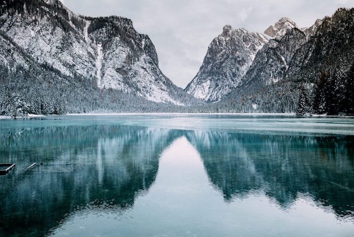 lake surrounded by mountain peaks, tall trees on both sides, covered with snow, winter background