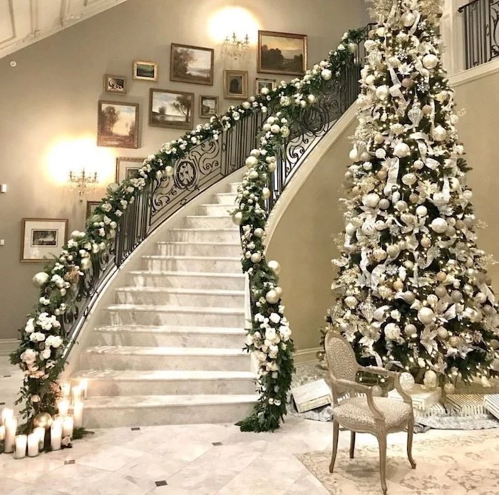 tall tree next to a large staircase, decorating christmas tree with ribbon, decorated with white and silver ornaments and flowers