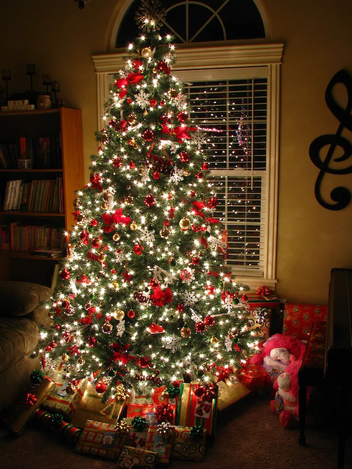 tree decorated with lots of lights, red and gold ornaments and bows, decorating christmas tree with ribbon, presents underneath
