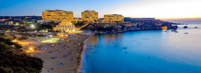 north golden bay in malta, large hotels on the seaside on top of large rocks, beautiful beaches, photo taken at sunset