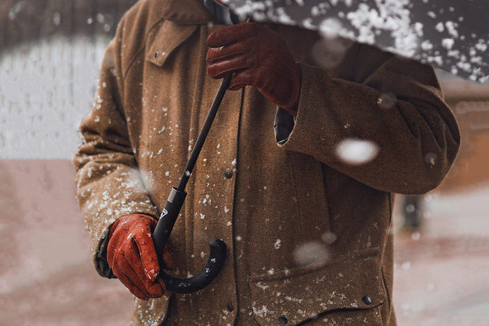 man holding a black umbrella, wearing brown coat and brown leather gloves, christmas gift ideas for boyfriend, snow falling