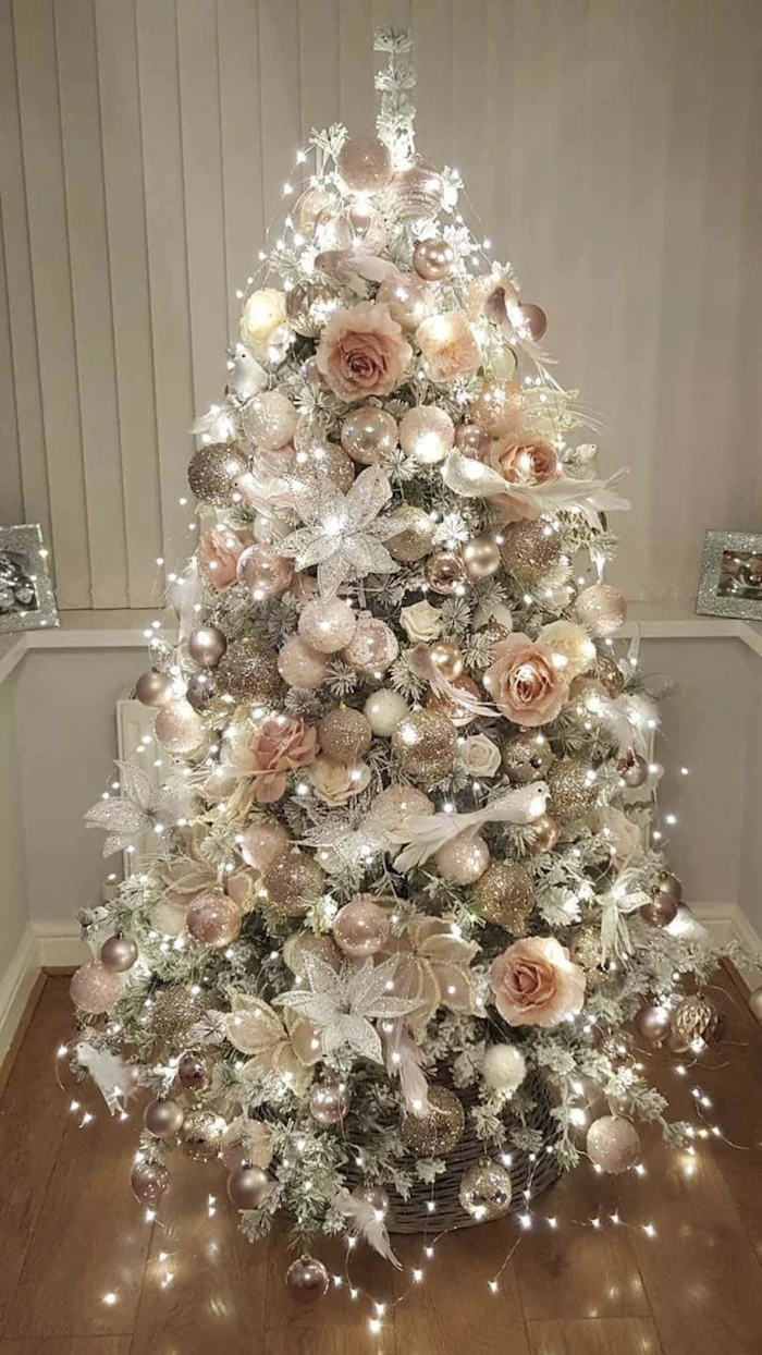 white christmas tree decor, rose gold and silver ornaments, faux flowers and lots of lights on a tree, placed on wooden floor