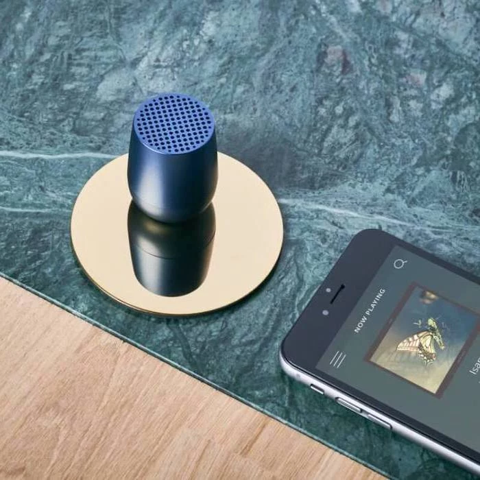 blue mini wireless speaker, placed on golden coaster, next to a phone playing music, good gifts for boyfriend