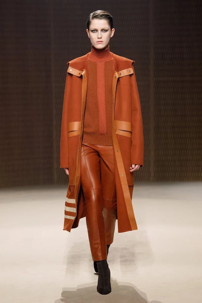 clothing trends, model walking down a runway, wearing brown leather pants, orange sweater and long coat