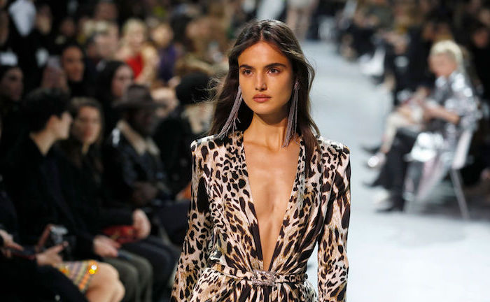 leopard print dress with deep plunge neckline, worn by model on the runway, clothing trends, people sitting in the background
