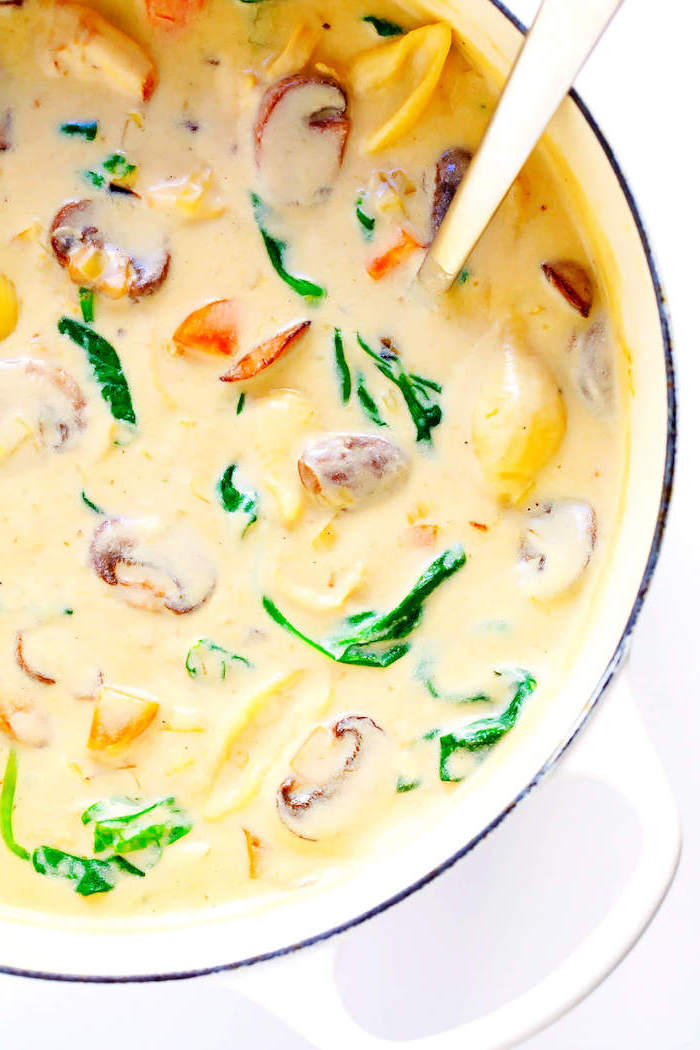 white pot full of soup, mushrooms and spinach inside, creamy tortellini soup, white background