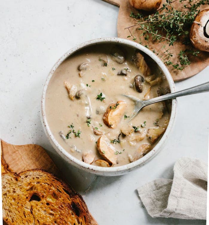 grey ceramic bowl full of soup, mushrooms and croutons inside, fresh herbs on the side, creamy tortellini soup