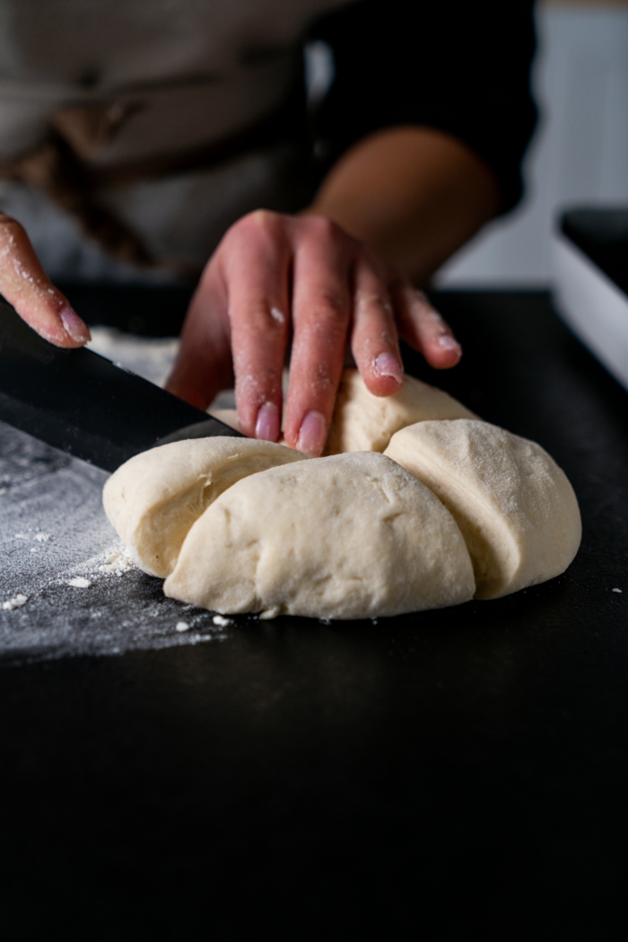 naan bread recipe, dough being cut in four with sharp knife, placed on black surface, covered with flour