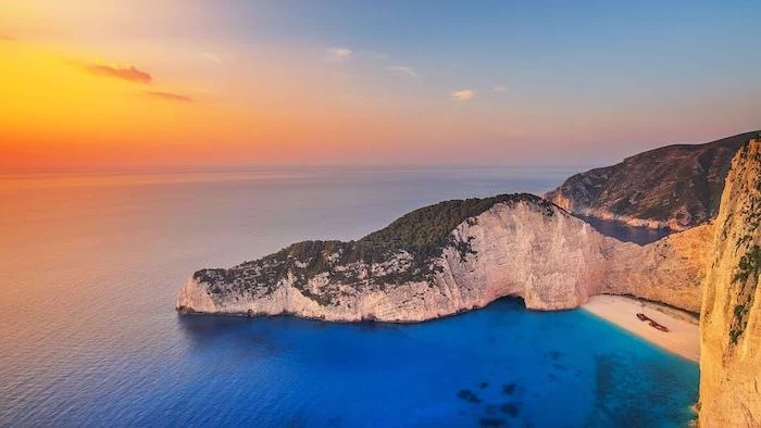 large rock going all the way into the water, beautiful beaches, navagio beach in greece, clear turquoise water