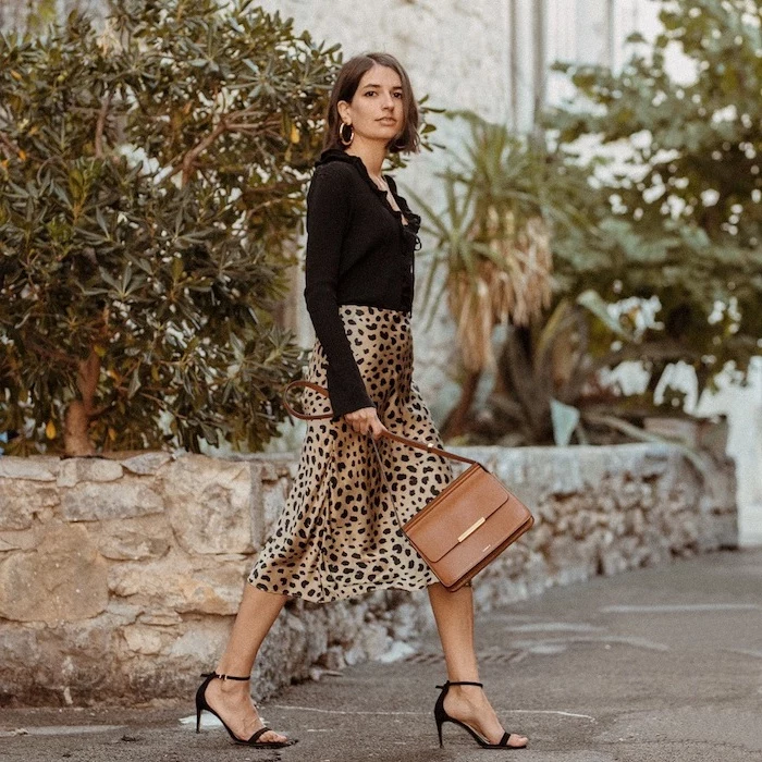 woman walking down the street, wearing silk leopard print skirt and black blouse, black sandals, winter fashion for women