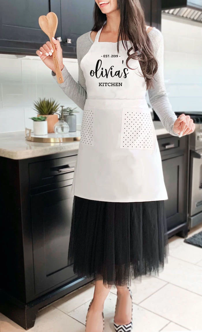 olivia's kitchen personalised apron, worn by woman with black hair, christmas presents for moms, standing in the middle of a kitchen