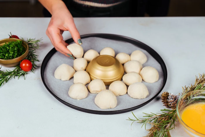 small dough balls, placed on paper lined baking sheet, pull apart christmas bread, golden bowl in the middle