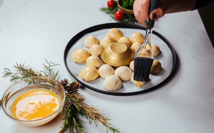 small dough balls, covered with beaten eggs, pull apart christmas bread, arranged on paper lined baking sheet