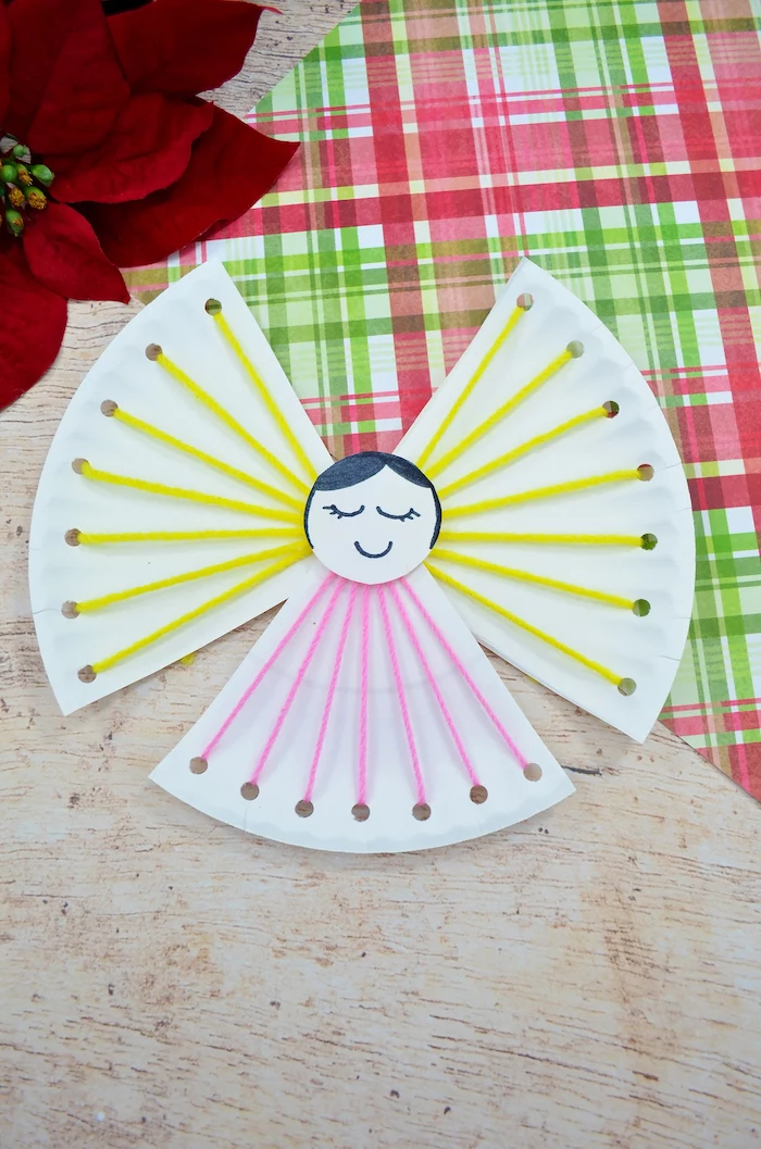 paper plate angel, made with yellow and pink yarn, diy christmas crafts, placed on a wooden surface