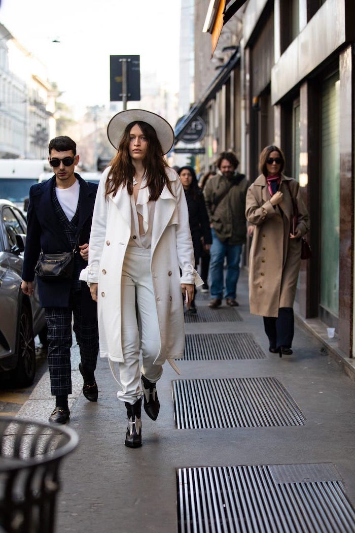 people walking down the street, 2019 clothing trends, woman wearing white pants and blouse, long white coat and hat