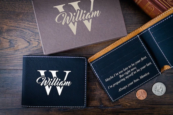 christmas gift ideas for him, personalised wallet with love message inside, made of black leather, placed on wooden surface