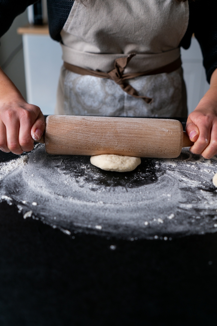 dough being rolled out, naan bread recipe, placed on black surface, covered with flour
