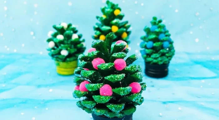 pinecones painted green, colorful pompoms glued to it, diy christmas ornaments for kids, pinecone christmas trees