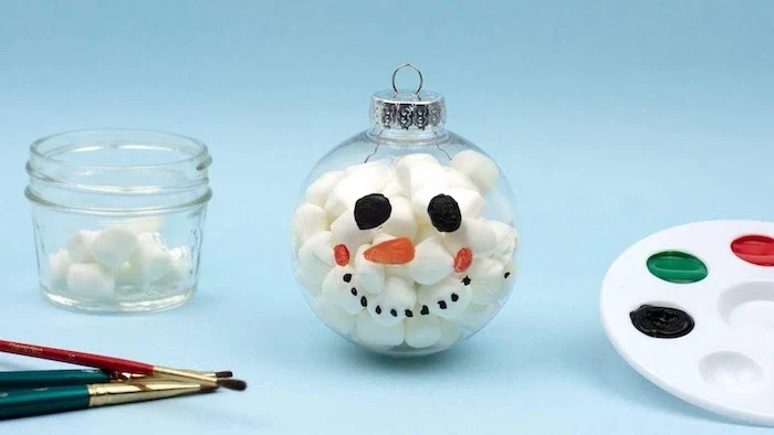 plastic bauble filled with cotton balls, diy christmas crafts, snoman face painted on it, diy christmas crafts, placed on blue surface