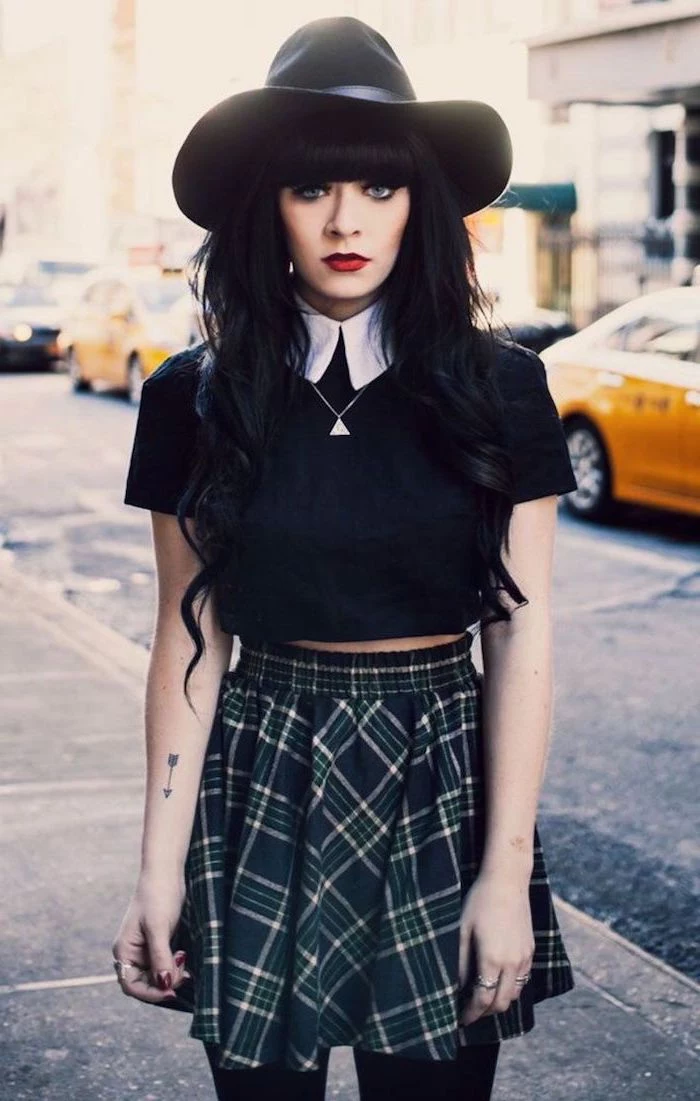 woman with black hair with bangs, wearing plaid pleaded skirt, 2019 clothing trends, black crop top and hat