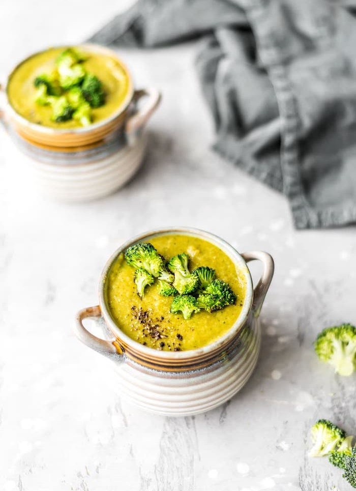 homemade cream of chicken soup, two ceramic bowls full of soup, broccoli on top for garnish, grey table cloth