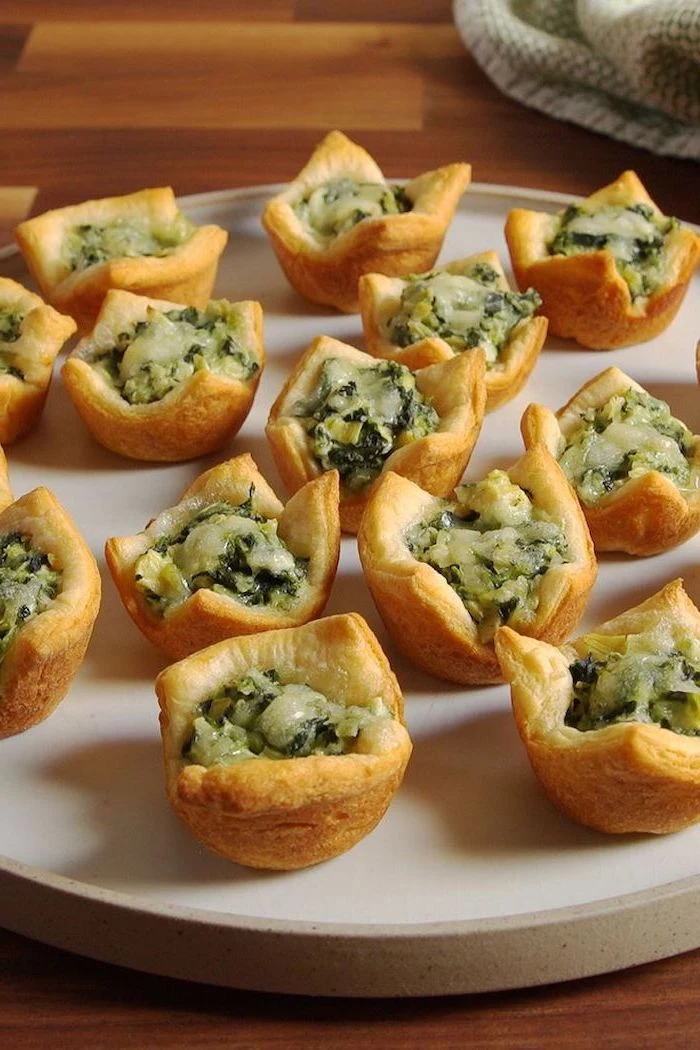 puff pastry filled with spinach and artichoke, easy holiday appetizers, arranged on white plate, placed on wooden surface