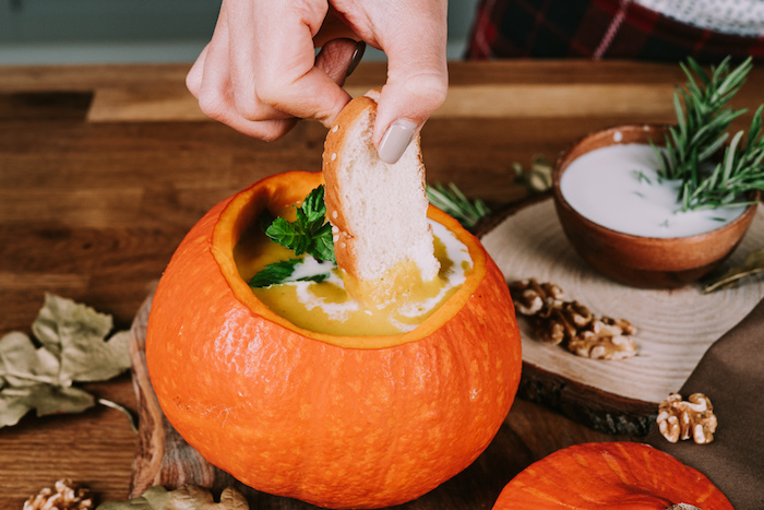 pumpkin soup poured inside a carved pumpkin, bread dipped in the soup, easy soup recipes, wooden table arrangement