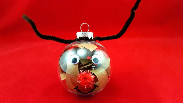 plastic bauble filled with paper, christmas ornament crafts, turned into a reindeer, placed on red surface