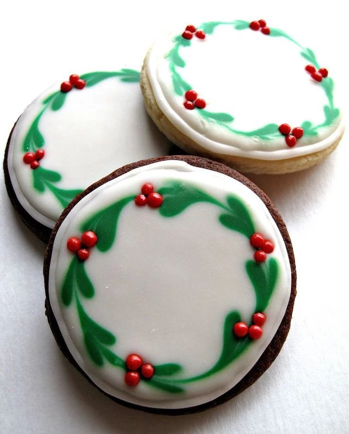 round cookies with wreaths drawn on them, using white and green icing, christmas cookie icing, placed on white surface